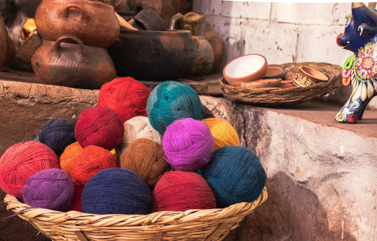 Colorful yarn balls in a rustic basket with Peruvian pottery and crafts in a traditional setting.